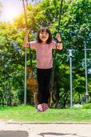 Cute little girl having fun on a swing in beautiful summer garden. Child girl playing on outdoor playground in park. Active summer leisure for kids photo