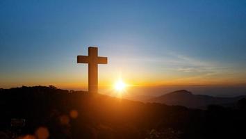 siluetas de cristiano cruzar símbolo en parte superior montaña a amanecer cielo antecedentes. concepto de crucifixión de Jesús Cristo. foto