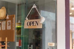 A business sign that says Open on local businesses hang on door at entrance. Say Welcome. Open and closed flip sign in front of shop glass door. photo