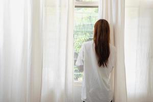 Woman in white nightgown waking up on weekend morning resting and relaxing playing with laptop mobile phone Eating bread and drinking tea in glass inside white bedroom.  Morning vacation concept. photo