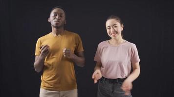 multietnico giovane amici danza su nero sfondo. asiatico donna e africano giovane amico danza e avendo divertimento su nero sfondo. video