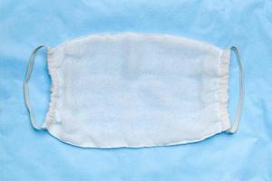 Handmade protective surgical face mask made from white sterile cheesecloth on blue medical background photo