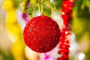 Glowing red Christmas ball and colorful shining tinsel hanging on branch of tree. Close-up view Xmas festive composition for Happy New Year photo