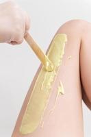 Closeup hand in glove applying hot wax on woman leg using spatula. Professional depilation procedure photo