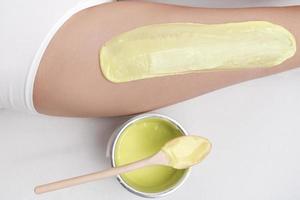 Cropped view from above of green hot wax on woman leg while she lying down on couch photo
