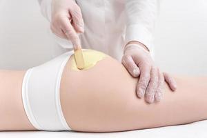 Unrecognizable beautician in gloves applying hot wax on buttocks using spatula. Waxing procedure photo