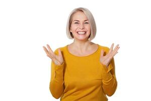 Middle aged blonde emotionally posing in a studio. Happy woman in yellow bright sweater on white background photo