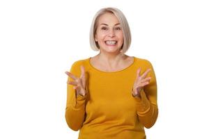 Middle aged blonde emotionally posing in a studio. Happy woman in yellow bright sweater on white background photo