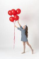 Girl holding in hand red balloons, other hand reaches for balloons and standing on tiptoes on white photo