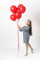 Nosy girl holding bunch of red balloons in two hands and looking at balloons on white background photo