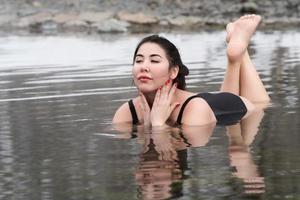 Full figured model in black swimsuit lying and relaxation in mineral water in outdoors pool at spa