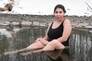 Outsize young adult woman in black swimming costume sitting and bathing in in outdoors pool at spa photo