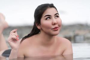 Happy plus size young woman lying down and relaxation in water of outdoors pool at geothermal spa photo