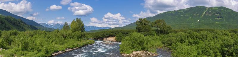 Panorama view of beautiful summer landscape - stream water of mountain river and green forest on sunny day with white clouds in blue sky photo