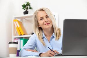 mujer de negocios que trabaja en la oficina con documentos. hermosa mujer de mediana edad mirando a la cámara con una sonrisa mientras se sienta en la oficina. foto