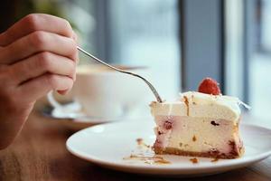 Woman have breakfast at cafe, eating raspberry cheesecake with coffee photo