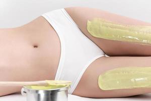 Legs of slim woman while she lying down on couch during depilation process with green hot wax photo