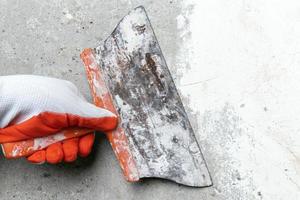 Hand of plasterer holds old trowel, scrubbing concrete wall, removes old plaster during redecoration photo