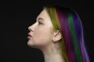 perfil de un joven hembra modelo con Perfecto sensual labios y multicolor hebras de pelo en un negro antecedentes. hermosa facial piel, aumento de hembra labios, atractivo elegancia. foto