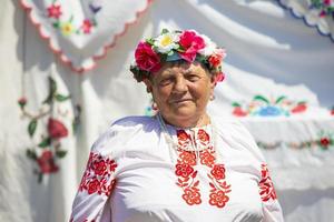 An elderly Belarusian or Ukrainian woman in national clothes against the background of towels. Slavic ethnic grandmother. photo
