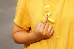 asiático mujer participación amarillo cinta a cofre nivel en amarillo antecedentes de camisa. el amarillo cinta simboliza esperanza, esperando y reunión. por lo tanto, eso es usado como un símbolo de hueso cáncer. foto