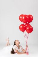 Beautiful girl on birthday holiday party, lying down and holding red balloons in hand, looking up
