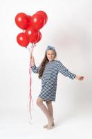Girl holding bunch of red balloons in hand, looking at camera. Full length model on white background
