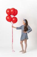 Girl in striped dress holding large bunch of red balloons on outstretched hand and looking at them photo