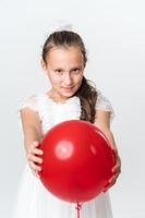 Front view of playful girl holding out red balloon with both hands and looking at camera photo