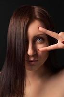 Portrait of brunette woman showing victory sign near eye and looking at camera photo