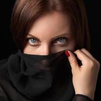 Portrait of shy woman covering her mouth and nose or face with scarf and looking at camera photo