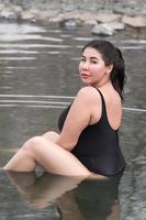 Overweight young woman in black swimsuit sitting in outdoors pool at spa, looking over shoulder photo