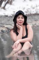 Plus size busty young woman in black bathing swimsuit sitting in outdoors pool at spa resort photo