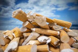 Cigarette stubs dropped and left in a pile on a beautiful beach photo