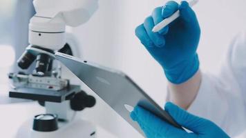 medisch wetenschap laboratoriumportret van mooi zwart wetenschapper op zoek onder microscoop doet analyse van test steekproef. ambitieus jong biotechnologie specialist, werken met Geavanceerd uitrusting video