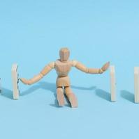 A wooden puppet toy holds back a falling domino on a blue background, representing the concept of a strong personality photo