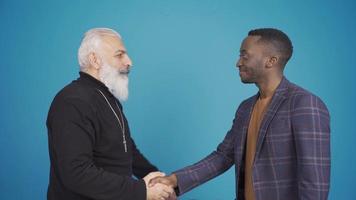 Christian man and muslim african young man shaking hands and hugging each other. Muslim and Christian men looking at camera with happy faces. video