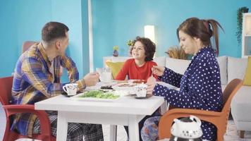 The cheerful and lively family is having their breakfast and the little boy is making his family laugh. Cute handsome boy telling jokes and jokes to his mom and dad at the breakfast table. video
