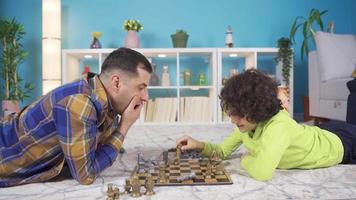 The boy is preparing to eat his father in chess, they are having fun with each other. Loyal and loving father playing chess with his son at home and they are happy. video