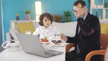 reifen Geschäftsmann haben Frühstück mit seine Sohn während Arbeiten auf Laptop. Geschäftsmann und Junge haben Familie Frühstück im das Morgen, chatten, Vater Portion seine Sohn zu essen. video