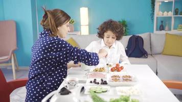 le mère, qui fait du sa peu garçon petit-déjeuner, fait du lui boisson Lait et aide lui à aller à école après petit déjeuner. video