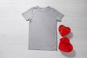 Grey tshirt mockup. Valentines Day concept shirt, gift boxes heart shape on wooden background. Copy space, template blank front view t-shirt clothes. Romantic outfit. Flat lay holiday fashion photo