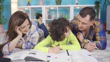 Adult parents help their primary school student sons with their lessons. Parents helping with homework by lying on the carpet at home. Child education concept. video