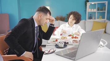 triste soltero empresario teniendo desayuno con su hijo en el Mañana. soltero empresario experimentando cansado y Estresante dias es teniendo desayuno con su niño y trabajando en el ordenador portátil. video