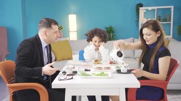 Parents qui avoir petit déjeuner dans le Matin faire leur malheureux les enfants rire et divertir. le grincheux garçon à le petit déjeuner table est remarqué par le sien parents, et le Parents faire lui rire et acclamation en haut. video