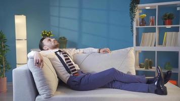 Thoughtful and tired cool stylish young man lying on sofa. The handsome businessman has a unique style of dressing and lifestyle. Thoughtful elegant businessman lying on sofa and resting. video