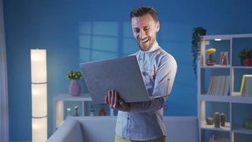 contento elegante uomo Lavorando remoto su il computer portatile mentre danza e avendo divertimento a casa. bello e carismatico uomo d'affari guardare a il computer portatile a casa e avendo divertimento mentre ballando. video