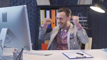 elegante bello uomo seduta nel ufficio sedia e utilizzando computer, gioia che cosa lui vede su schermo, festeggiare vittoria. video