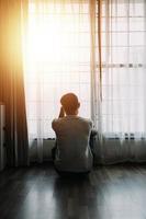 Alone man silhouette staring at the window closed with curtains in bedroom. Man stands at window alone photo