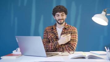 gelukkig mannetje leerling aan het studeren Bij bureau en op zoek Bij camera glimlachen en uitdrukken gelukkig aan het studeren. de intelligent en vastbesloten mannetje leerling, wie geniet aan het studeren. video